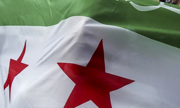 Image of a protester stands behind a Syrian Republic flag as Syrian refugees and local residents take part in a demonstration against Syria's President Bashar Al-Assad, after Friday prayers outside the Syrian embassy in Amman March 30, 2012.