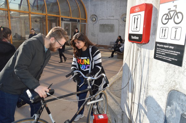 Image of two people trying to fix their bike with tools at the Bicycle repair stop outside the entrance of Dupont subway 