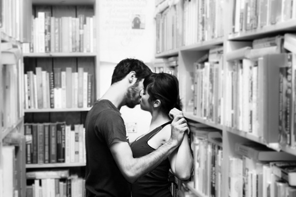 Image of a couple kissing against the library shelf