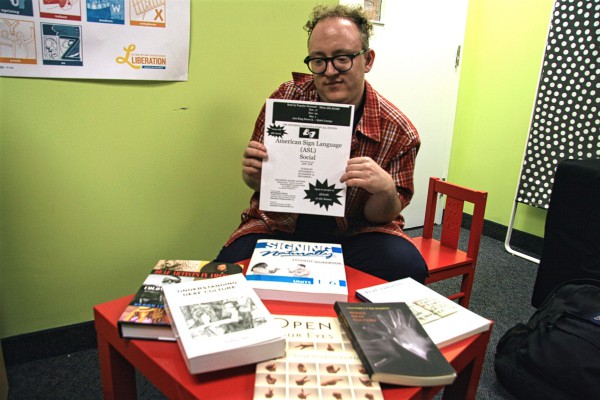 Image of Maverick Smith, facilitator of the ASL socials in the Community Action Centre office holding the poster