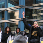 Photo of a woman with her arm in the air holding a microphone speaking to a Black Lives Matter Toronto rally on March 26