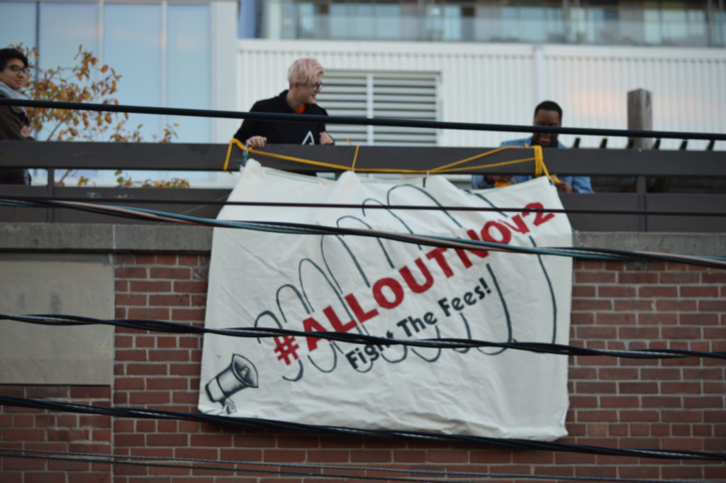 "Members of the Community Action Centre unfurl a large banner in support of the Fight the Fees! Campaign" Photo: Malcolm Derikx / The Dialog