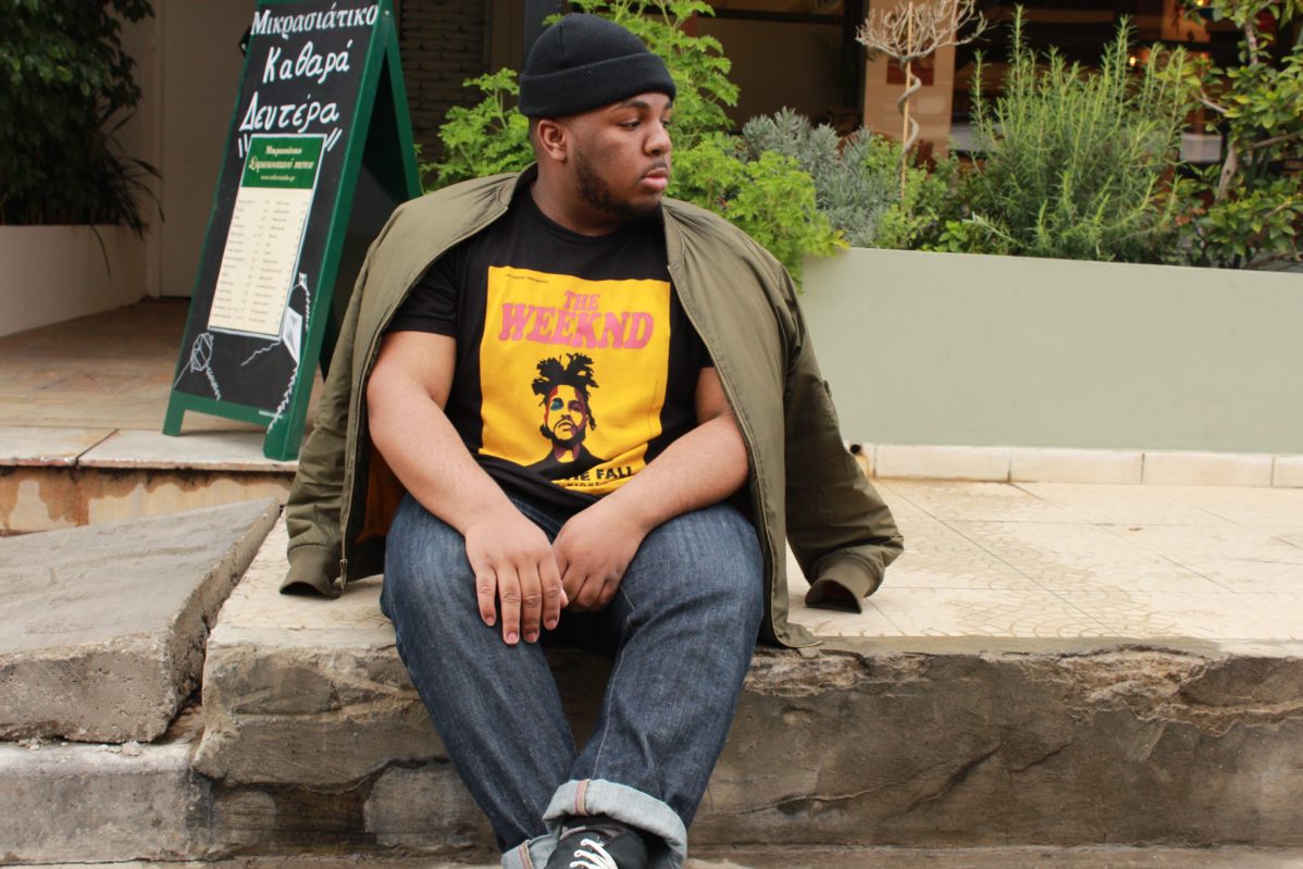 Clayson Fletcher, a GBC fashion management student, sits on a rock with a T-shirt of The Weekend and a jacket draped over his shoulders. Photo courtesy of Clayson Fletcher.