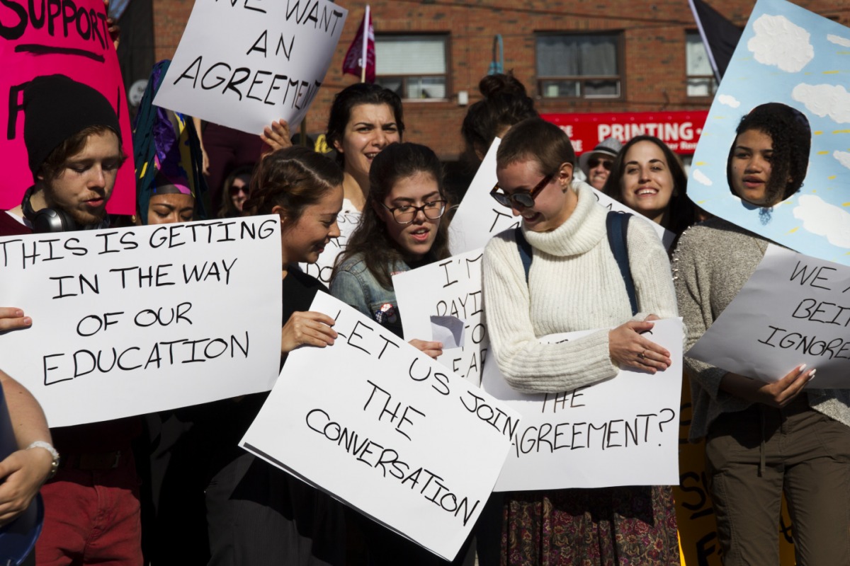 Students look at their chant sheet and hold their signs at Humber College’s Lakeshore Campus on Friday, October 20, 2017. The chant included lines like “We’re mad at the college, not at our teachers” and “This is not fair, just get it together.” Photo: Kit Kolbegger / The Spare