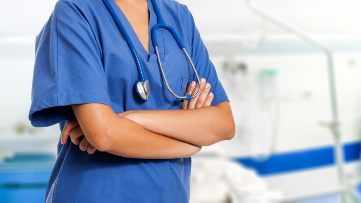 A nurse in blue scrubs against a blurred background
